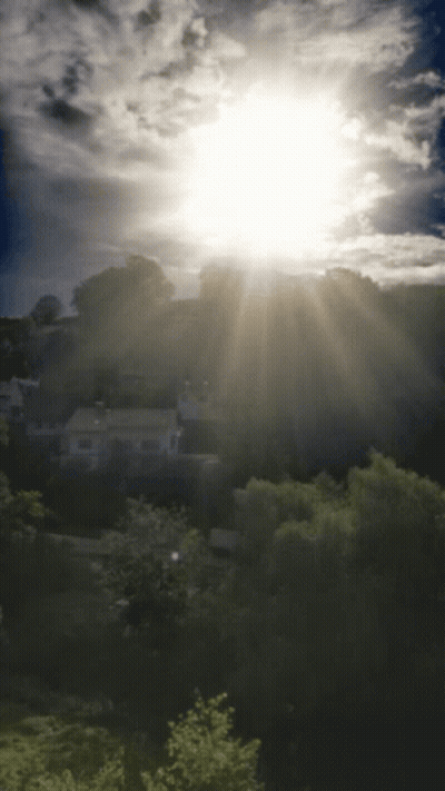The Sun Is Shining Brightly Through The Clouds Over A Residential Area GIF