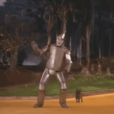 The Tin Man From The Wizard Of Oz Is Dancing On The Yellow Brick Road With A Dog . GIF