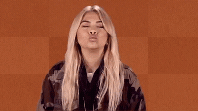 The Woman Is Wearing A Camouflage Jacket And Blowing A Kiss . GIF