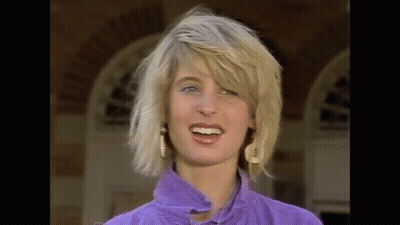 The Woman Is Wearing A Purple Shirt And Earrings And Is Smiling . GIF