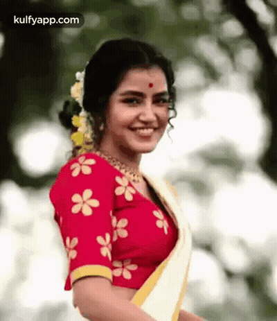 The Woman Is Wearing A Red Blouse With Yellow Flowers On It And A White Saree . GIF