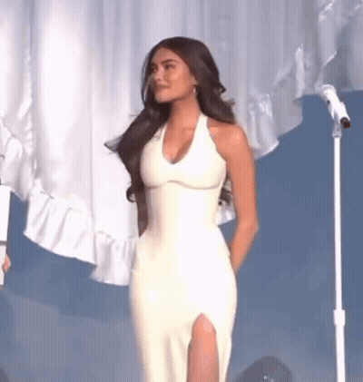 The Woman Is Wearing A White Dress And Standing In Front Of A Microphone . GIF
