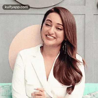 The Woman Is Wearing A White Jacket And Smiling While Sitting On A Couch . GIF