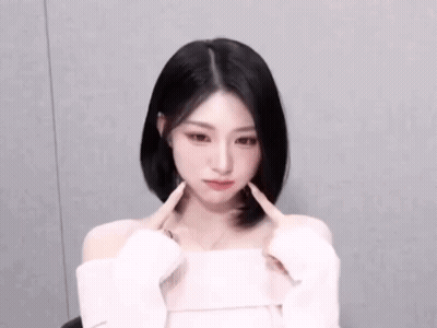 The Woman Is Wearing A White Off The Shoulder Top And Making A Heart Shape With Her Hands . GIF