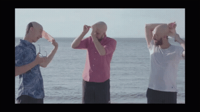 Three Bald Men Are Standing On The Beach With Their Heads In The Air GIF