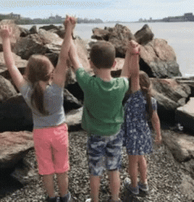 Three Children Are Standing On A Rocky Beach Holding Hands GIF