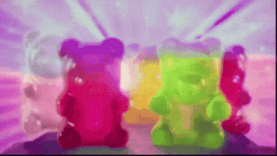Three Colorful Gummy Bears Are Sitting Next To Each Other On A Pink Surface GIF