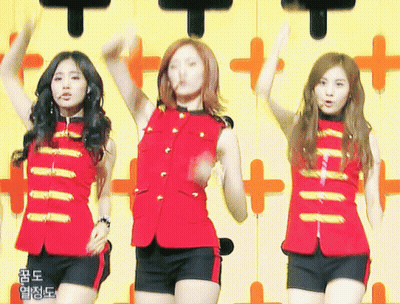 Three Girls Are Dancing In Front Of A Yellow Wall With Chinese Writing GIF