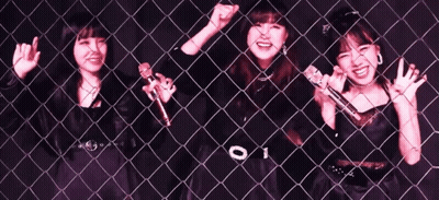 Three Girls Are Singing Into Microphones Behind A Chain Link Fence GIF