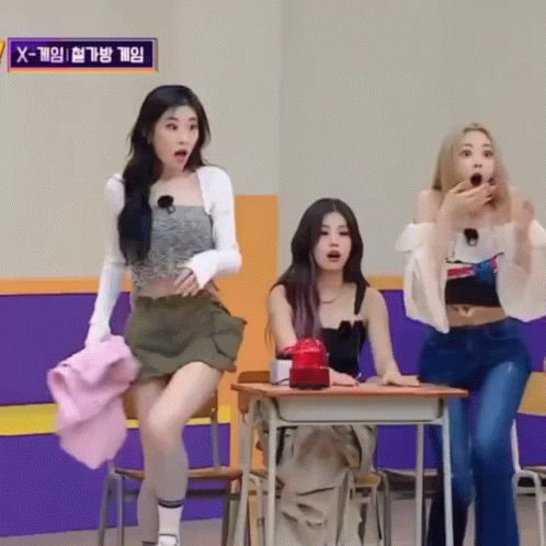 Three Girls Are Sitting At Desks In A Room With A Sign That Says X-Game . GIF