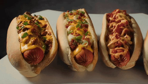 Three Hot Dogs With Different Toppings On Them GIF