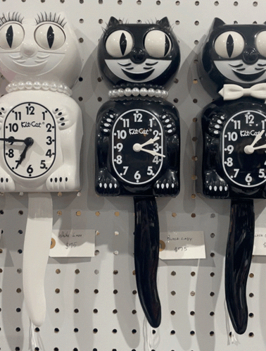 Three Kitsch Cat Clocks Are Lined Up On A White Wall GIF