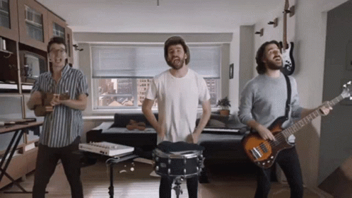 Three Men Are Playing Instruments In A Living Room Including A Drummer And A Guitar Player GIF