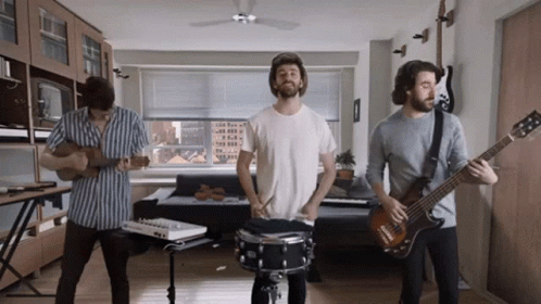 Three Men Are Playing Instruments In A Living Room Including A Drummer GIF