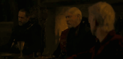 Three Men Are Sitting At A Table In A Dark Room Talking . GIF