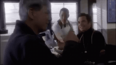 Three Men Are Sitting At A Table In A Room Talking To Each Other . GIF