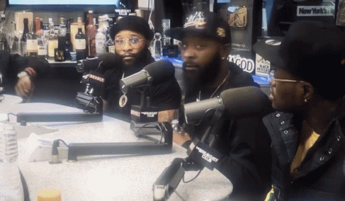 Three Men Are Sitting At A Table With Microphones In Front Of Them And A New York Times Sign In The Background GIF