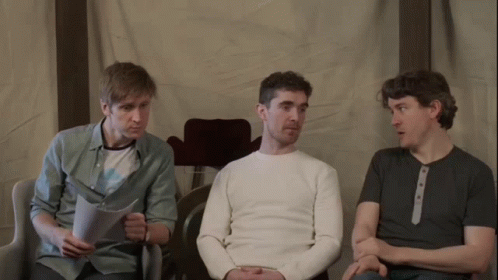 Three Men Are Sitting In Chairs And One Of Them Is Reading A Piece Of Paper GIF
