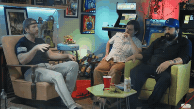 Three Men Are Sitting In Chairs In Front Of An Arcade Machine That Says Warrior On It GIF