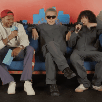 Three Men Are Sitting On A Couch And One Of Them Is Holding A Microphone GIF