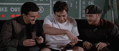 Three Men Are Sitting On A Couch In Front Of A Scoreboard And Laughing . GIF