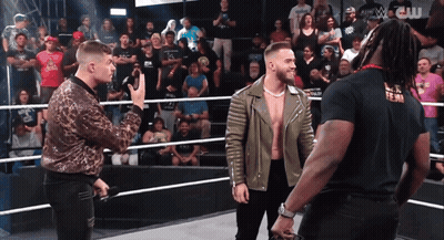 Three Men Are Standing In A Wrestling Ring And One Of Them Is Wearing A Black T-Shirt That Says W.c. GIF