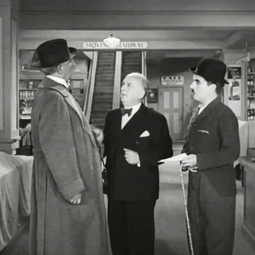 Three Men Are Standing In Front Of A Moving Stairway Sign GIF