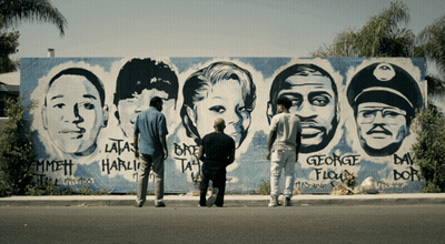 Three Men Are Standing In Front Of A Mural Of George Floyd 'S Face GIF