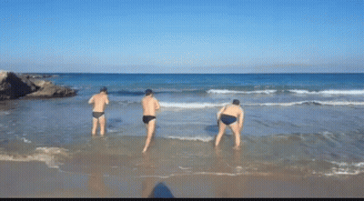 Three Men Are Standing In The Water On A Beach GIF
