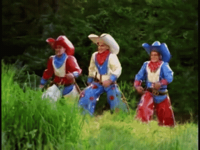 Three Men Dressed In Cowboy Costumes Are Standing In A Grassy Field GIF