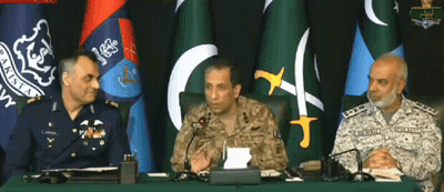 Three Men In Military Uniforms Sit At A Table With Microphones In Front Of Flags GIF