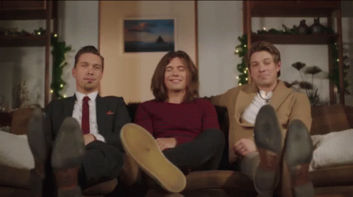 Three Men Sitting On A Couch With Their Feet On The Floor GIF