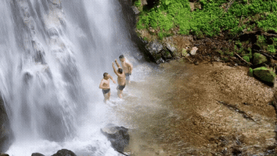 Three Men Swimming Under Waterfall Hands In Air GIF