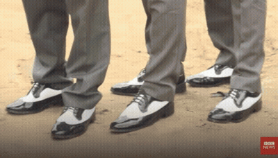 Three Men Wearing Suits And Black And White Shoes Are Standing Next To Each Other With Bbc News In The Corner GIF