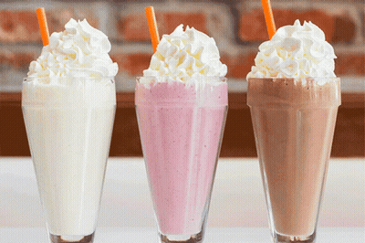Three Milkshakes With Whipped Cream And Straws On Top GIF