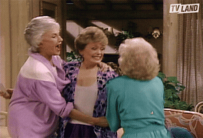 Three Older Women Are Hugging Each Other In Front Of A Tv Land Sign GIF