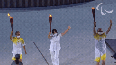 Three People Are Holding Torches In Front Of A Sign That Says ' Paralympic ' GIF