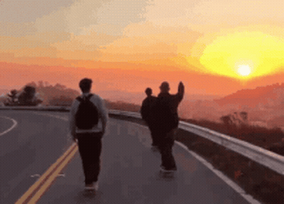 Three People Are Walking Down A Road At Sunset GIF