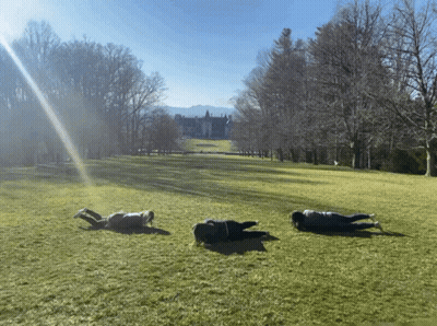 Three People Laying In Grassy Field With Large House GIF
