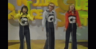 Three People Wearing Overalls With The Letter G On Them Singing Into Microphones GIF