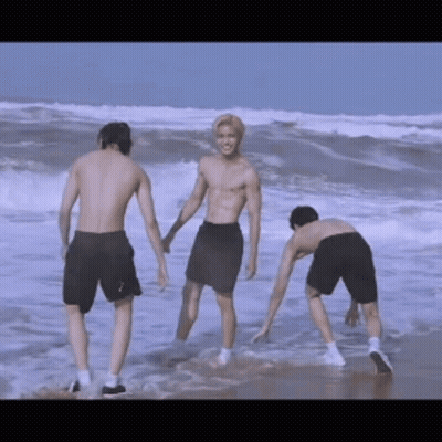 Three Shirtless Men Are Standing On The Beach Holding Hands GIF