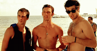 Three Shirtless Men Standing On Beach Talking GIF