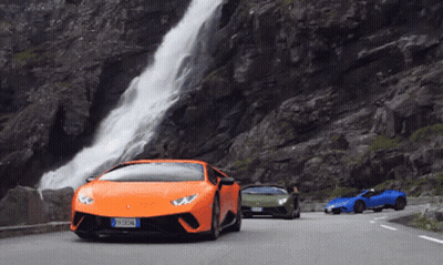 Three Sports Cars Are Driving Down A Road Near A Waterfall GIF