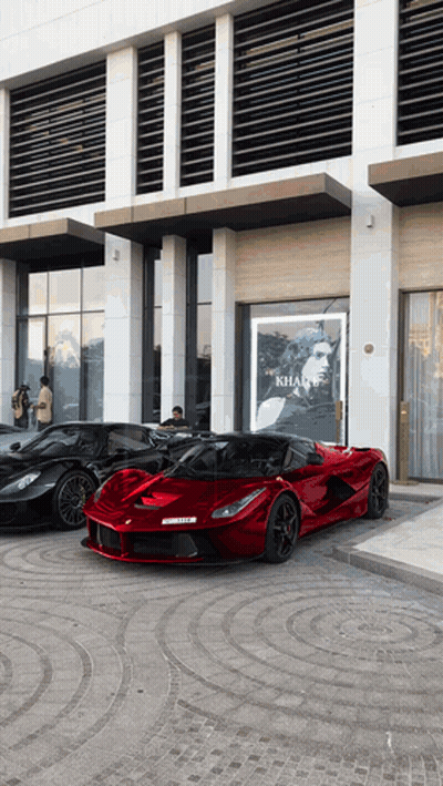 Three Sports Cars Parked In Front Of Khan Sign GIF