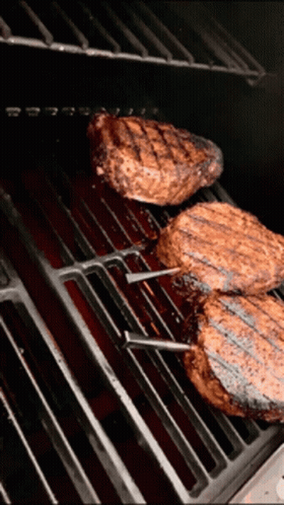 Three Steaks Are Cooking On A Grill With A Red Sauce GIF