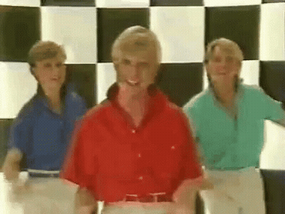 Three Women Are Dancing In Front Of A Checkered Wall . GIF