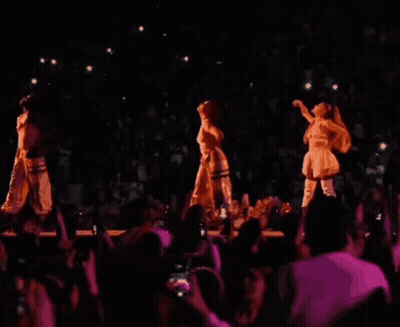 Three Women Are Dancing On A Stage In Front Of A Crowd In A Dark Room . GIF