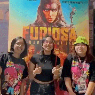 Three Women Are Posing In Front Of A Movie Poster That Says Furiosa GIF