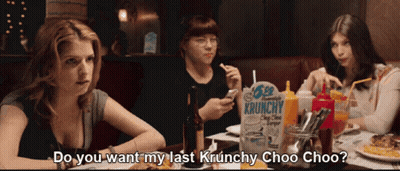 Three Women Are Sitting At A Table With A Box Of Krunchy Chips GIF