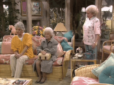 Three Women Are Sitting In A Living Room With Wicker Furniture GIF